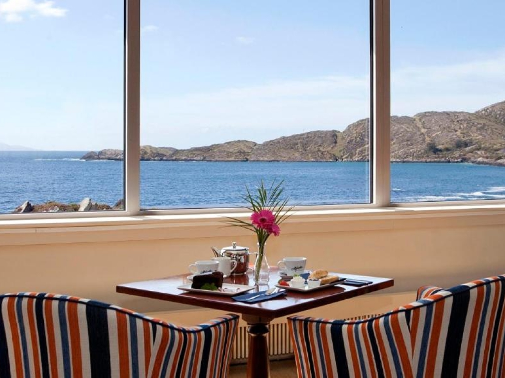 Pot of tea, cake and scones laid out on a table in front of a panoramic Atlantic Ocean window at the Derrynane Coast Hotel.