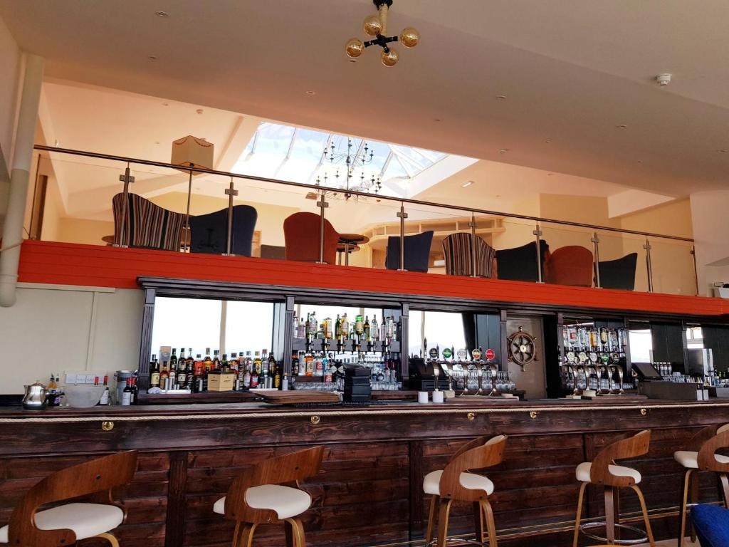 Long wooden cocktail bar with stools, ship's wheel detail and mezzanine seating at the Derrynane Coast Hotel.